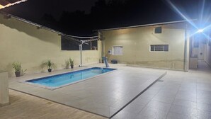 A swimming pool with a tiled deck, potted plants, and a building with a sloped roof. - House for 6. Private pool | Hot tub (Pindamonhangaba)