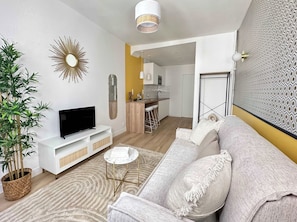 A modern living room with a flat-screen TV, a sofa, a small round table, and a potted plant. - Opera Cozy Studio by Melvane (Paris)
