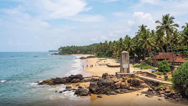 A beach with a stone monument, palm trees, and boats. - Townhouse Oak Thondayad Calicut Dream (Calicut)