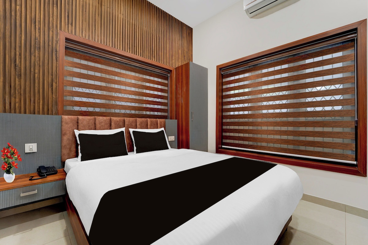 Une chambre d’hôtel moderne avec un grand lit, une tête de lit en bois et une vue à travers des stores en bois.
