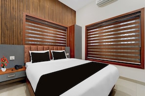 Une chambre d’hôtel moderne avec un grand lit, une tête de lit en bois et une vue à travers des stores en bois.