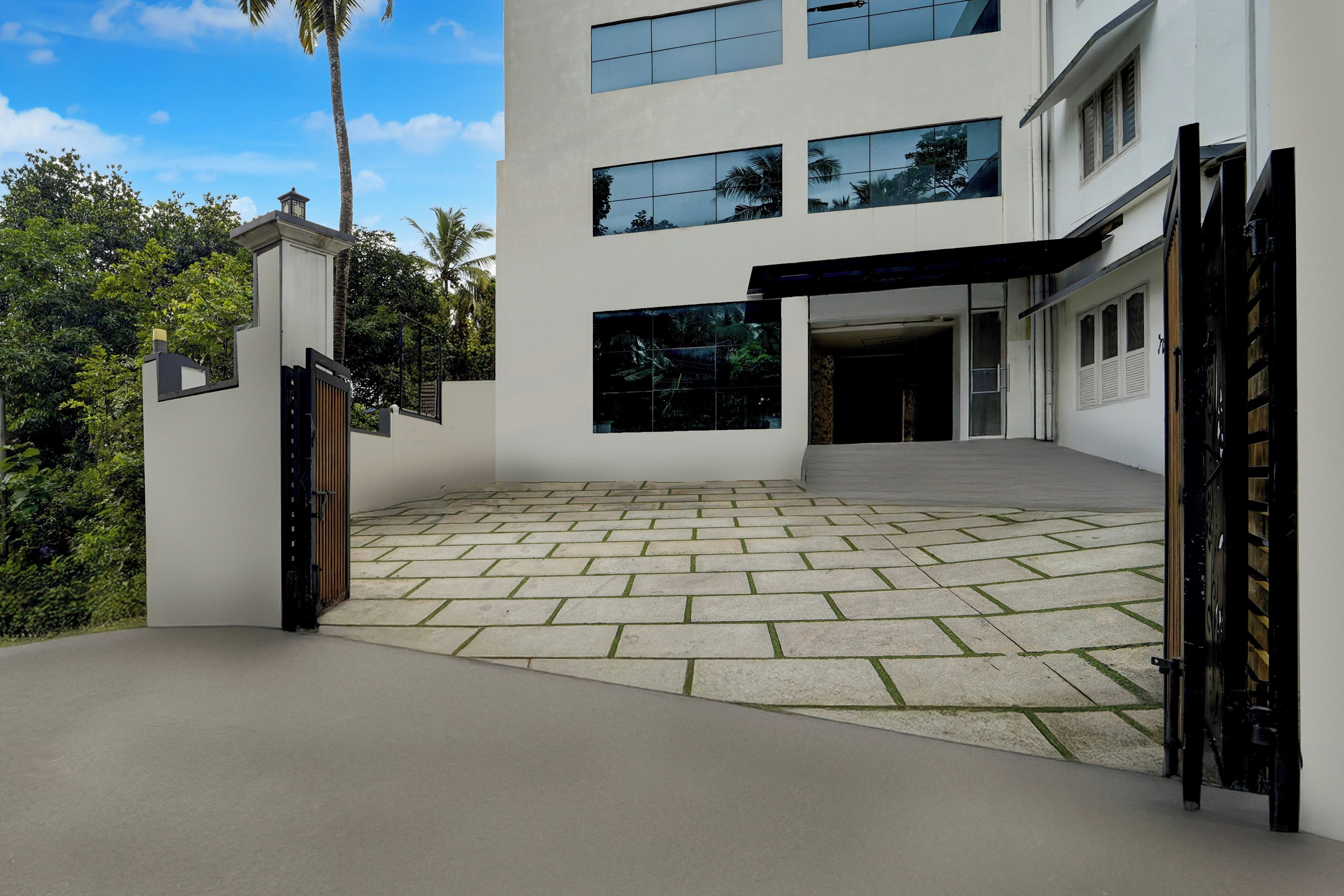 Un edificio moderno de dos pisos con un camino de entrada pavimentado y un acceso con portón.