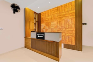 Un comptoir d’accueil avec une pancarte indiquant qu’il est géré par l’entreprise, un mur orné d’un motif géométrique en bois et une porte portant un numéro.