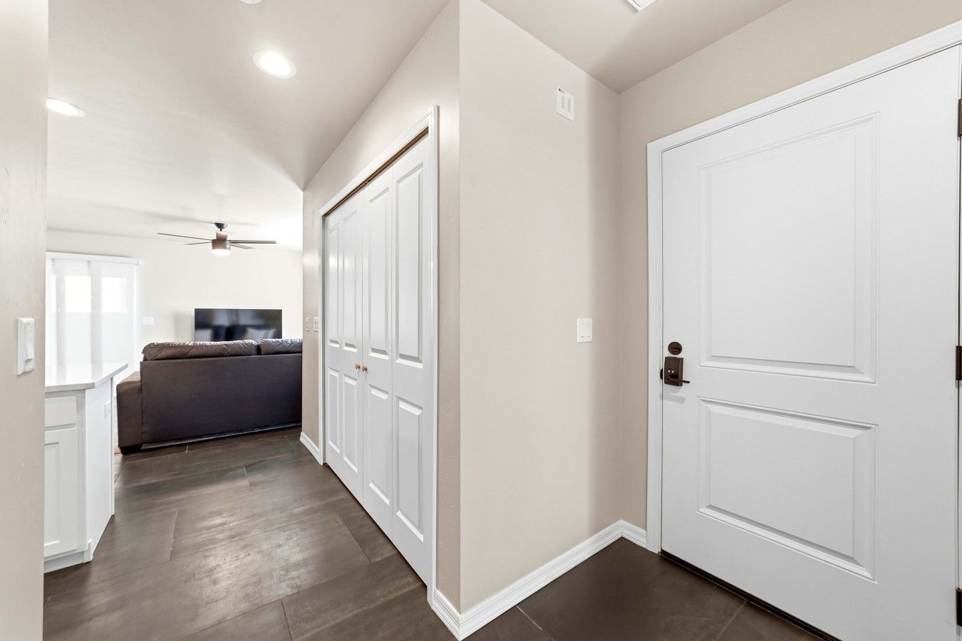A hallway with a ceiling fan, a grey sofa, and a white door.