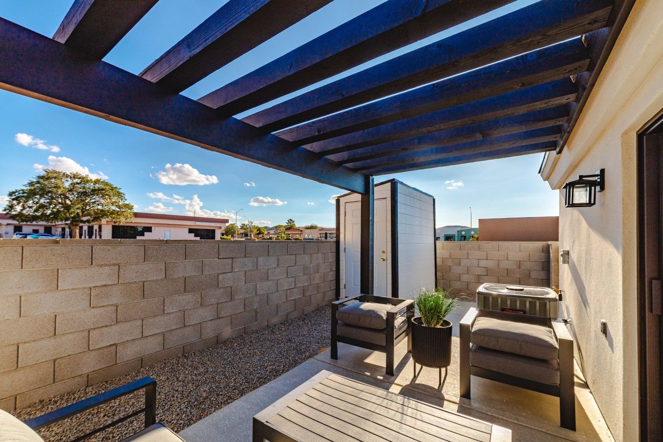 An outdoor patio with a pergola, seating area, and a small table with a plant.
