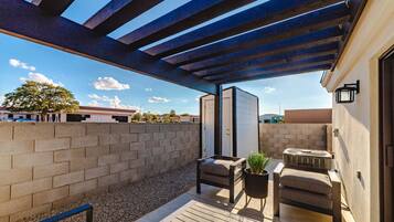 An outdoor patio with a pergola, seating area, and a small table with a plant.