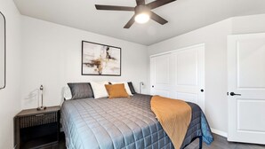 A bedroom with a bed, a ceiling fan, a nightstand, and a door. - Work-Ready Stay with Desk + ALLO Fiber WiFi (Kingman)