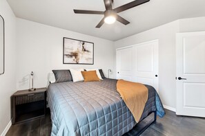 A bedroom with a bed, a ceiling fan, a nightstand, and a door. - Work-Ready Stay with Desk + ALLO Fiber WiFi (Kingman)