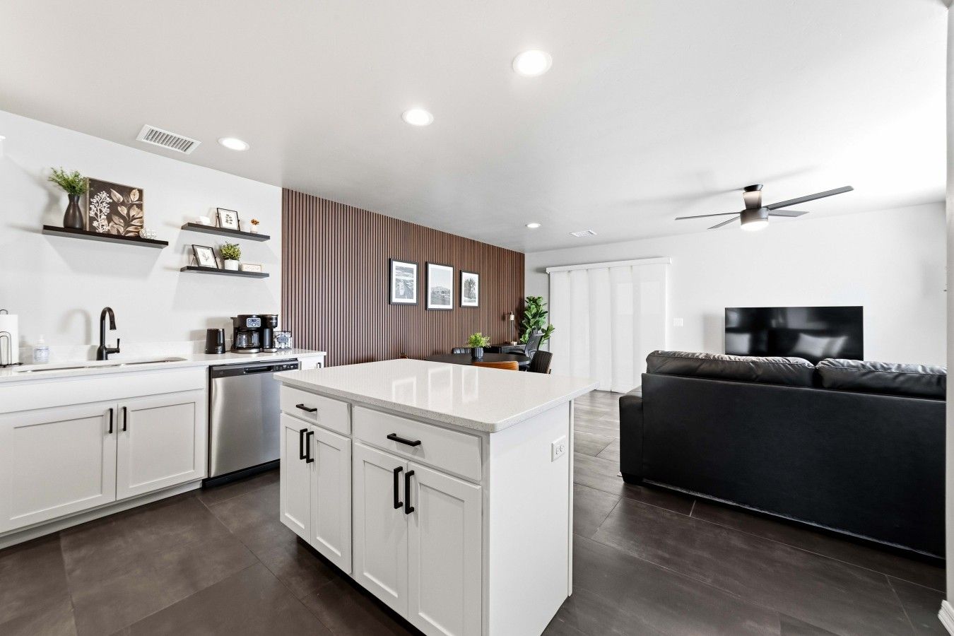 Una cocina moderna con armarios blancos, una isla central y una zona de comedor con un sofá negro.
