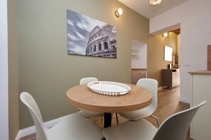 Ein Essbereich mit einem runden Tisch, weißen Stühlen und einem Wandbild des Kolosseums.