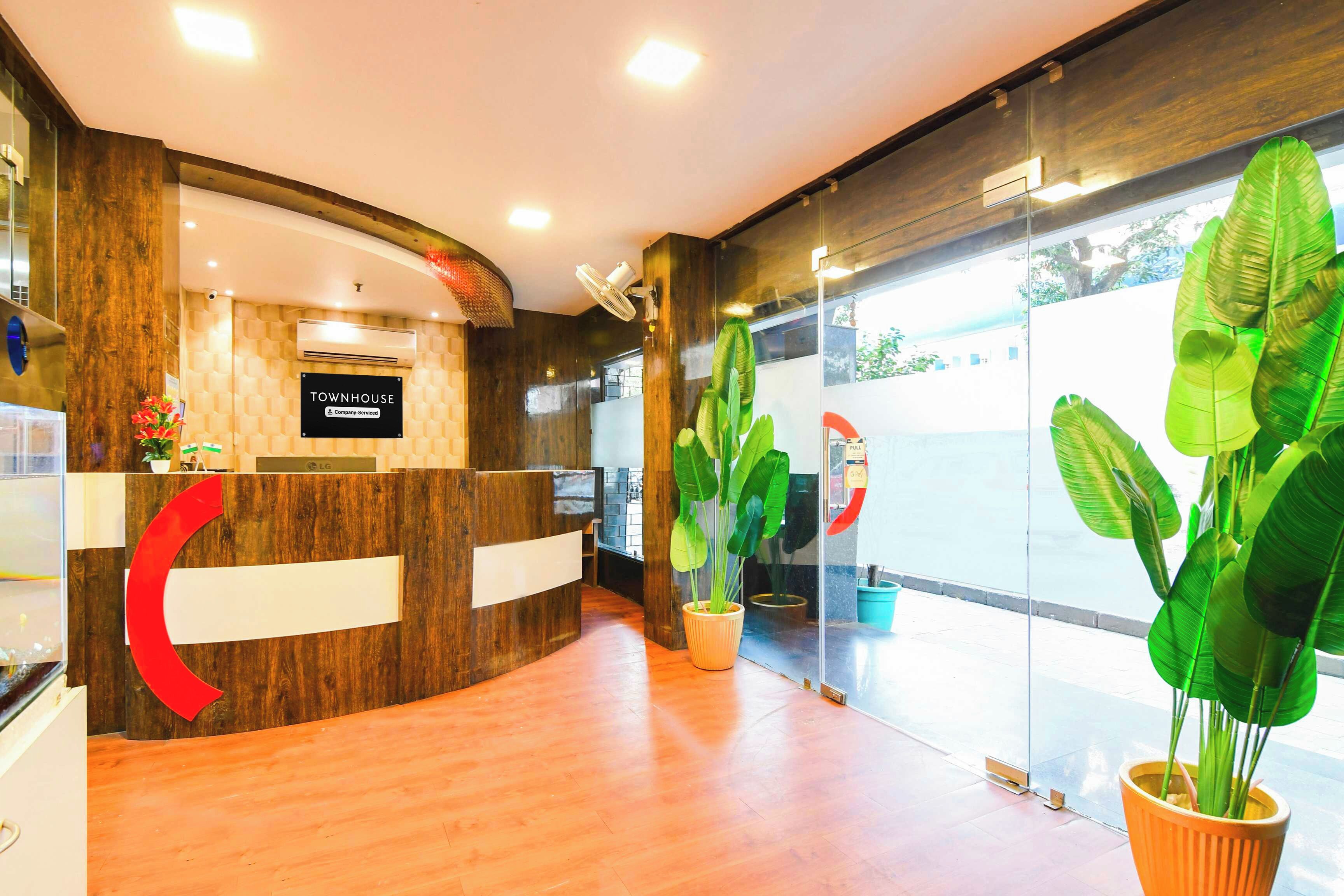 A reception area with a wooden reception desk, a sign indicating it is company-serviced, and a large potted plant.
