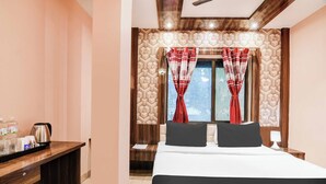 Une chambre d’hôtel avec un lit, une table de chevet avec une bouilloire, une commode et une fenêtre avec des rideaux.