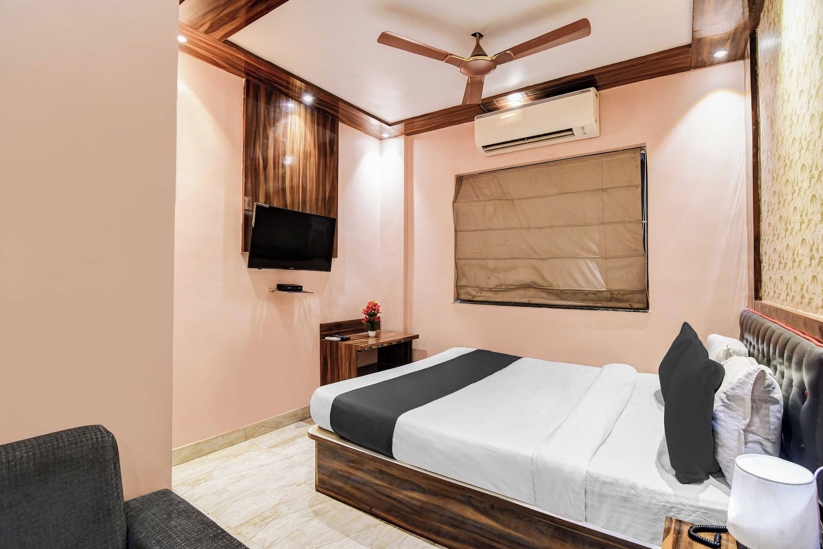 Ein Hotelzimmer mit Bett, Schreibtisch, Fernseher, Klimaanlage und Deckenventilator.