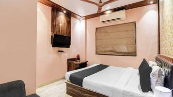 Ein Hotelzimmer mit Bett, Schreibtisch, Fernseher, Klimaanlage und Deckenventilator.