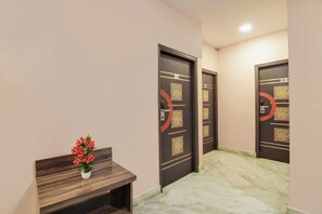 A hallway with marble flooring, a wooden bench with a potted plant, and doors with numbers and decorative patterns. - Townhouse Kolkata Rabindra Sadan Metro (Kolkata)
