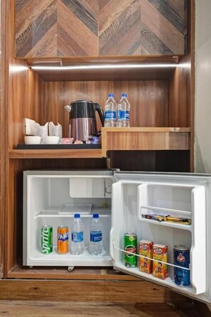 A kitchen area with a refrigerator, a coffee maker, and water bottles. - Hotel Saina International - Newly Built  (New Delhi)