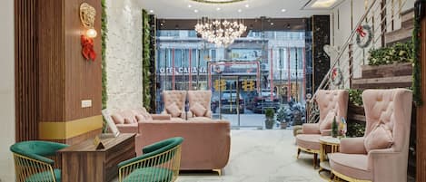 A hotel lobby with a central seating area, a staircase, and a view of the street.