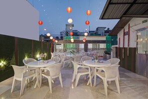 An outdoor seating area with white plastic chairs and tables, decorated with string lights and paper lanterns. - Hotel Saina International - Newly Built  (New Delhi)