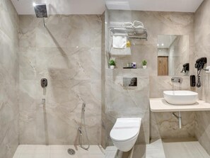 A modern bathroom with a glass-enclosed shower, a toilet, a sink with a mirror, and a towel rack. - Hotel Saina International - Newly Built  (New Delhi)
