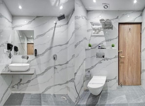 Un baño moderno con pared de mármol, puerta de madera, lavamanos blanco y un inodoro.