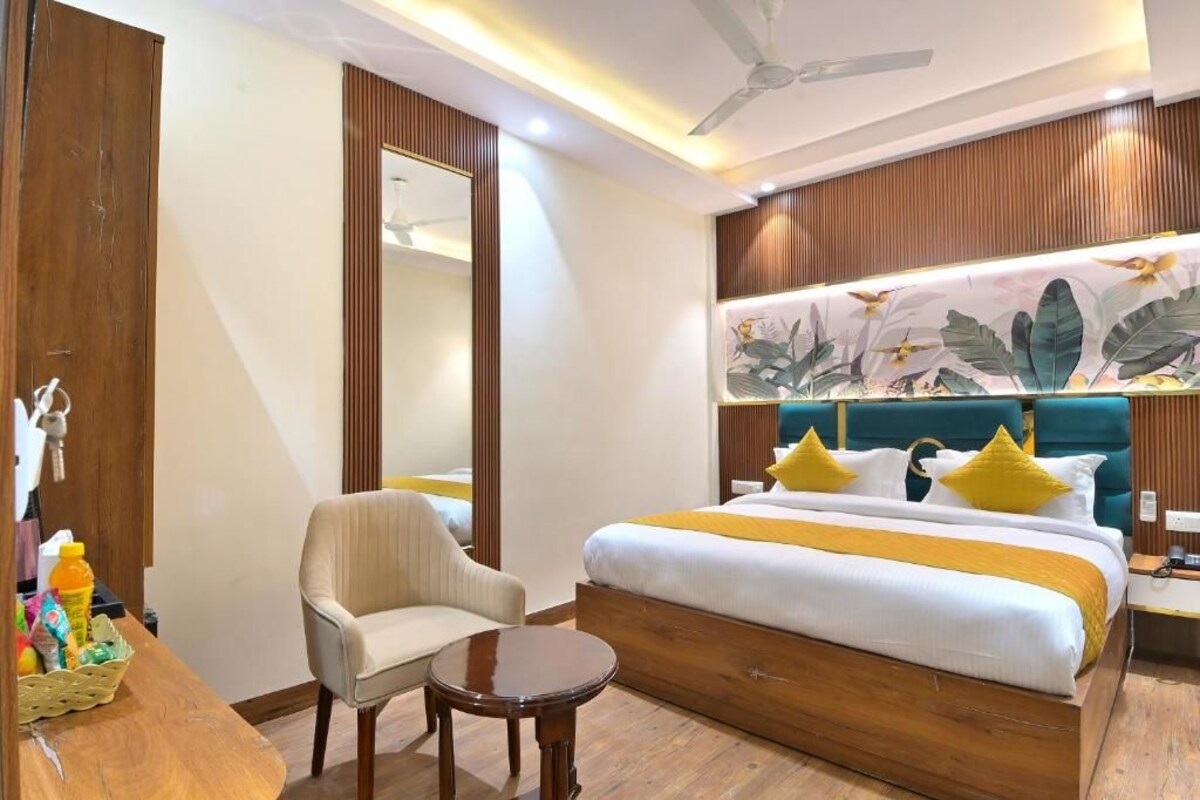 Een hotelkamer met een bed, een stoel, een klein tafeltje, een spiegel en een plafondventilator.