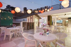 Un espace extérieur aménagé avec des tables et des chaises rondes, des guirlandes lumineuses et des lanternes rouges.