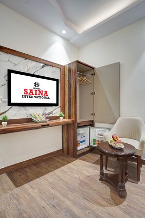 Une chambre d’hôtel avec un plancher en bois, un téléviseur fixé au mur, une petite table sur laquelle se trouve un bol de fruits et une chaise.