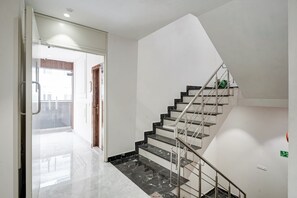 A modern interior with a marble staircase, a glass door entrance, and a view of the outside. - Hotel Saina International - Newly Built  (New Delhi)