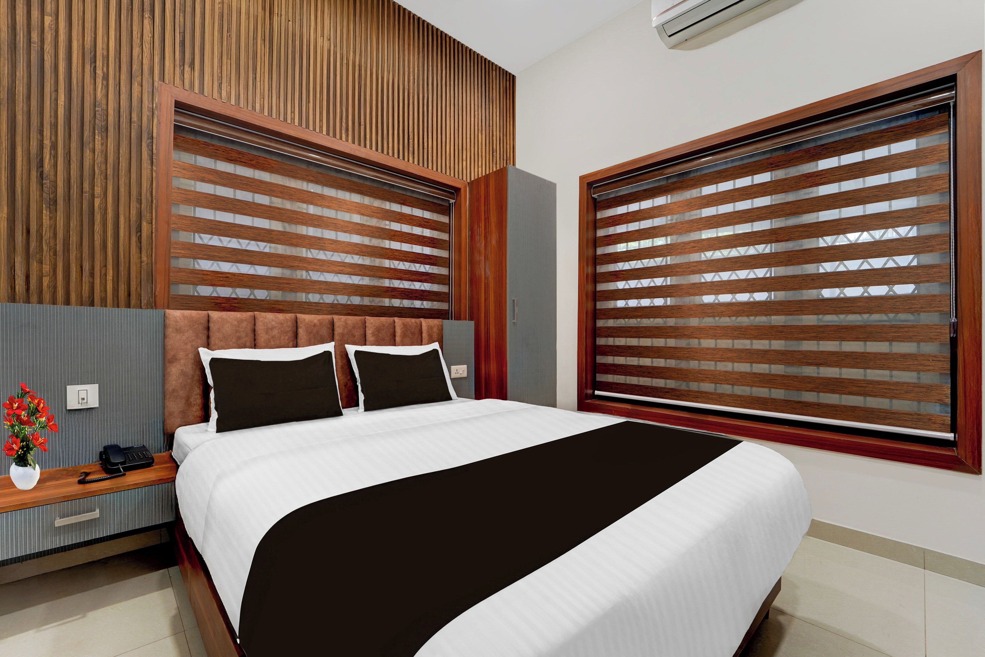 Una habitación de hotel moderna con una cama grande, cabecera de madera y una ventana con persianas.