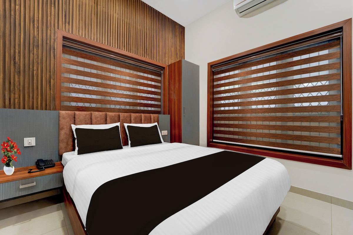 Une chambre d’hôtel moderne avec un grand lit, une tête de lit en bois et une fenêtre équipée de stores.