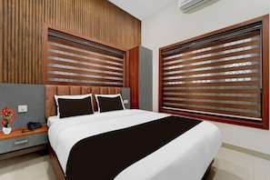 Une chambre d’hôtel moderne avec un grand lit, une tête de lit en bois et une fenêtre équipée de stores.