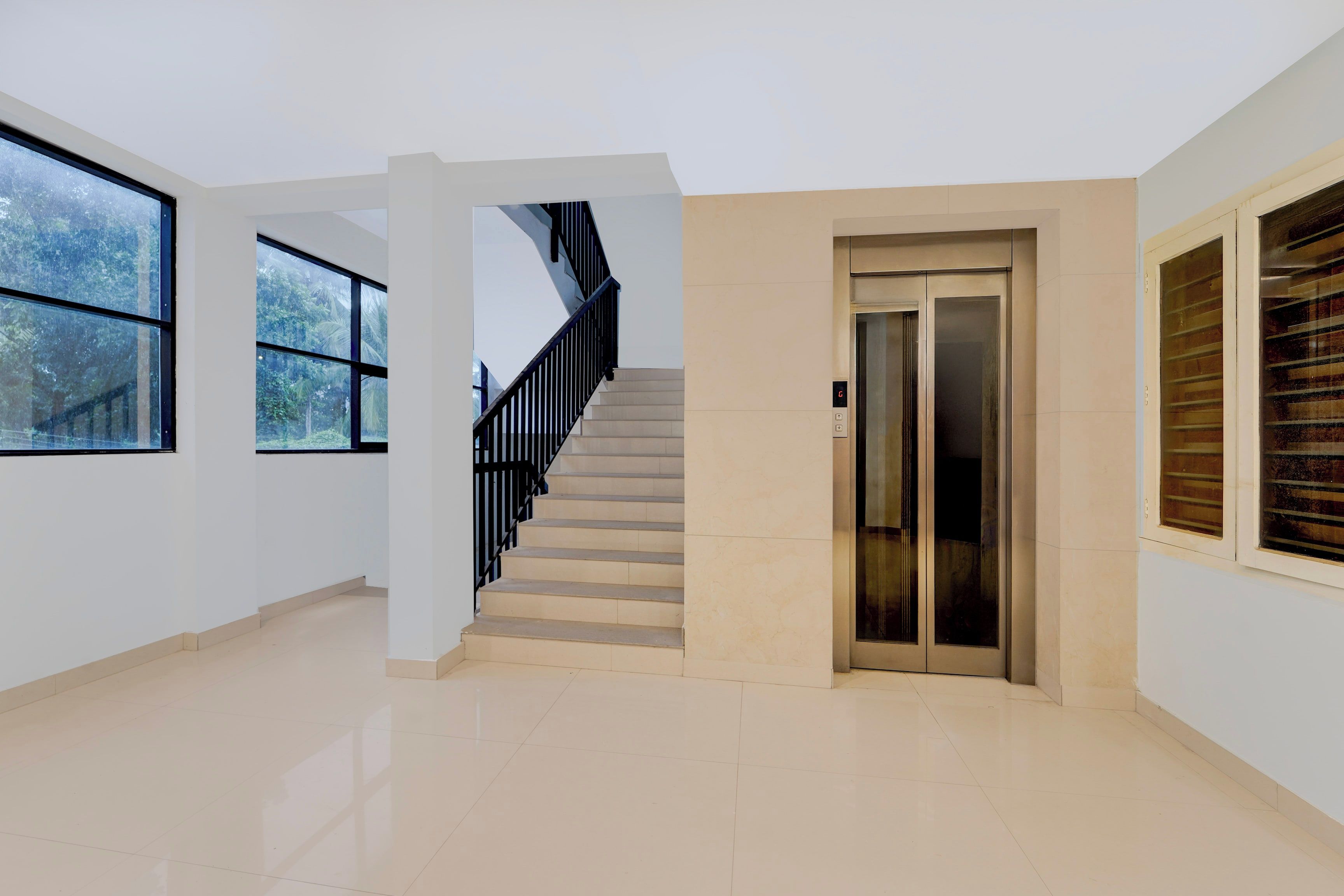 A spacious interior with a staircase, an elevator, and large windows.