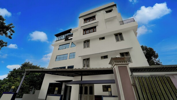 A multi-story building with a flat roof, large windows, and a balcony on the top floor.