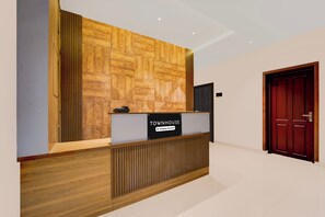 Un comptoir d’accueil avec une enseigne personnalisée, un mur recouvert de panneaux en bois et, au fond, une porte rouge.