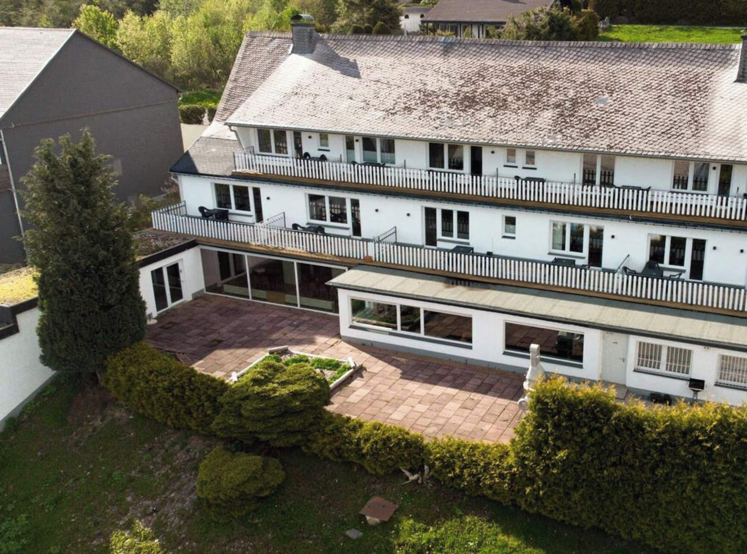 A two-story residential building with a balcony on the upper floor, a covered patio area, and a well-maintained garden.