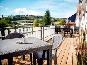 A wooden deck with a table and chairs, a white picket fence, and a view of a green landscape. - Holiday Apartment 705 (Winterberg)