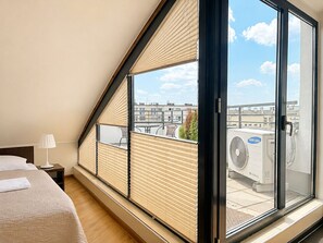 Ein Schlafzimmer mit großem Fenster, einem Bett, einem Nachttisch und Blick auf die Stadt.