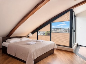 Un dormitorio con techo inclinado, una cama con ropa blanca y vistas amplias a través de un ventanal.