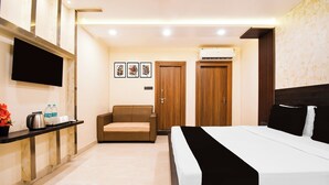 A hotel room with a bed, a sofa, a TV, a wall-mounted air conditioner, and a small table with a kettle and water bottles. - Townhouse Puri Former Hotel Narashingha (Puri)
