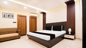 A bedroom with a bed, a bedside table, a lamp, a sofa, and two doors. - Townhouse Puri Former Hotel Narashingha (Puri)