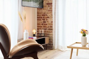 Ein modernes Wohnzimmer mit einer Ziegelwand, einem Flachbildfernseher über einem Kamin, einem Holzstuhl, einem kleinen Tisch mit Blumen und einem Bücherregal mit Büchern.