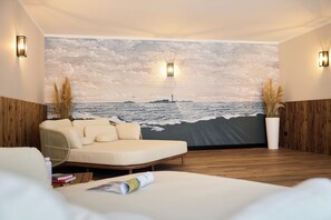 Ein modernes Zimmer mit einer großen Wandmalerei vom Meer, einer Couch und zwei Wandleuchten.