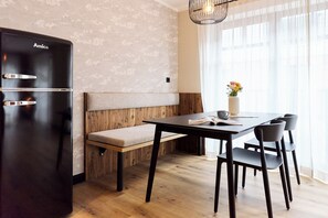 Una cocina moderna con un refrigerador negro, un banco de madera, una mesa de comedor con sillas y un florero con flores sobre la mesa.