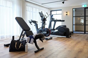Ein Fitnessraum mit Trainingsgeräten, einer Bank, einer Wasserflasche und einer Tasche auf dem Boden.