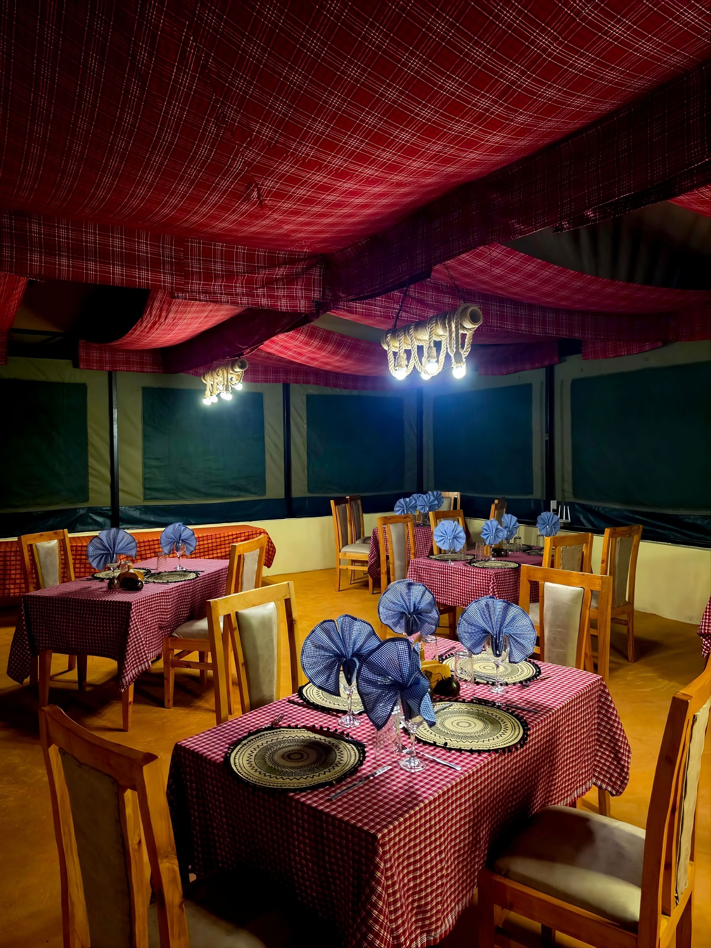 Un comedor con mesas dispuestas para varios invitados, con manteles a cuadros y centros de mesa azules.