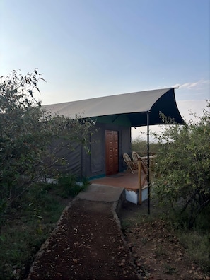 A small, single-story building with a covered porch and a door, surrounded by vegetation. - Awesome Masai Camp (Maasai Mara)