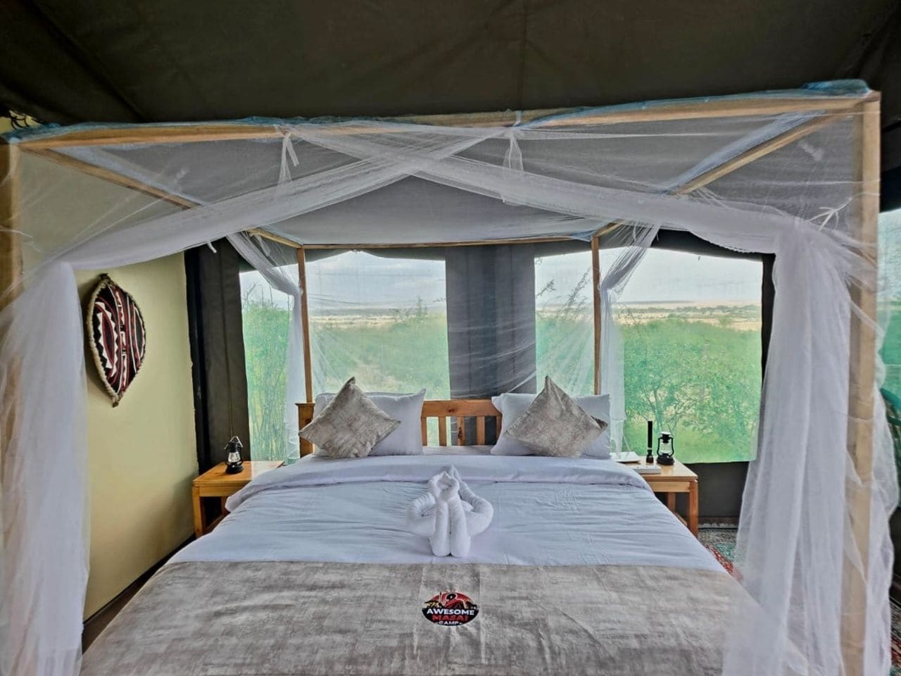 A bed with a canopy, pillows, a bedside table, and a view of greenery outside.