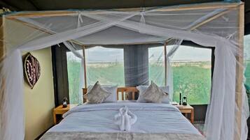 A bed with a canopy, pillows, a bedside table, and a view of greenery outside.