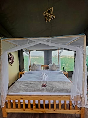 A tented room with a bed, a decorative hanging object, and a view of the outdoors. - Awesome Masai Camp (Maasai Mara)