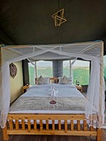 Una habitación con tienda de campaña, una cama, un adorno colgante y vistas al exterior.